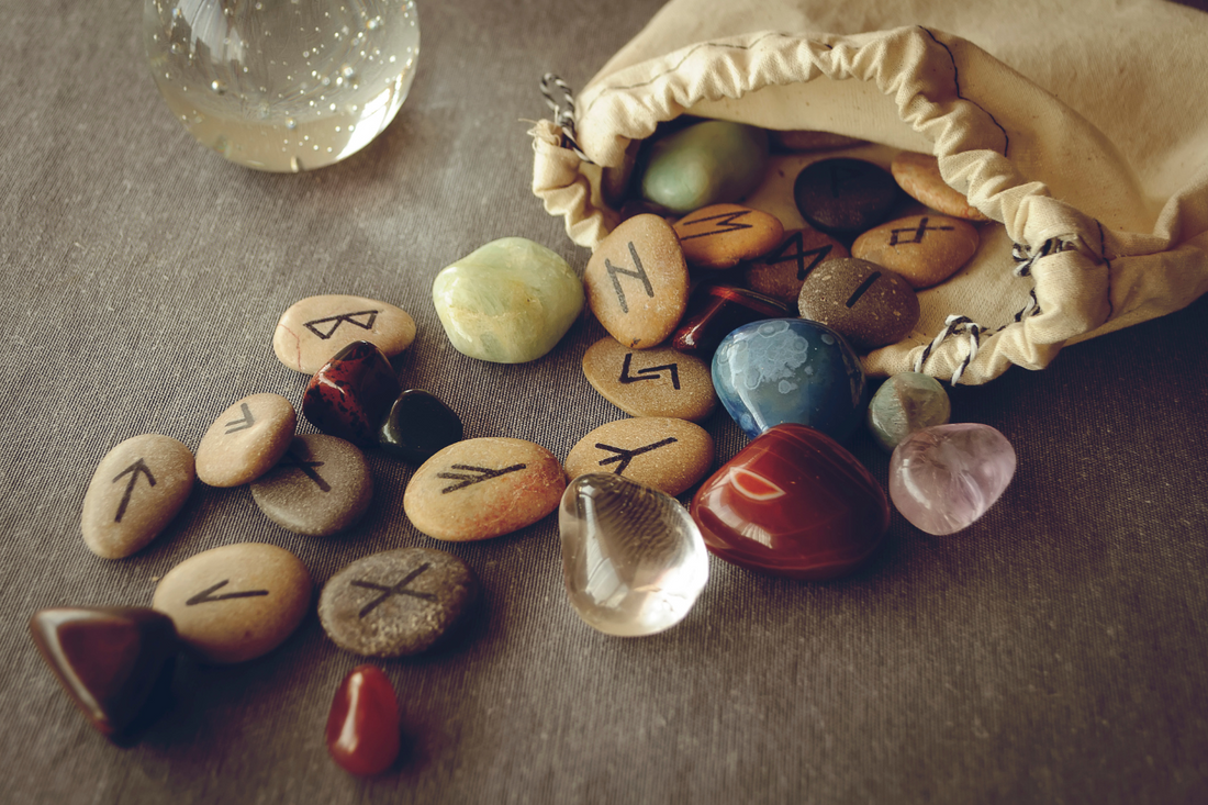 Ancient Norse runes carved on stones, scattered from a ritual bag alongside polished gemstones, representing Viking rune casting and mindfulness practices.