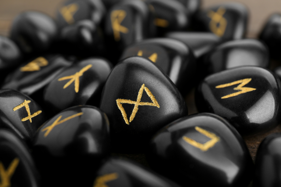 Close-up of glossy black rune stones etched with golden Norse symbols, evoking mysticism and sacred ritual practice.